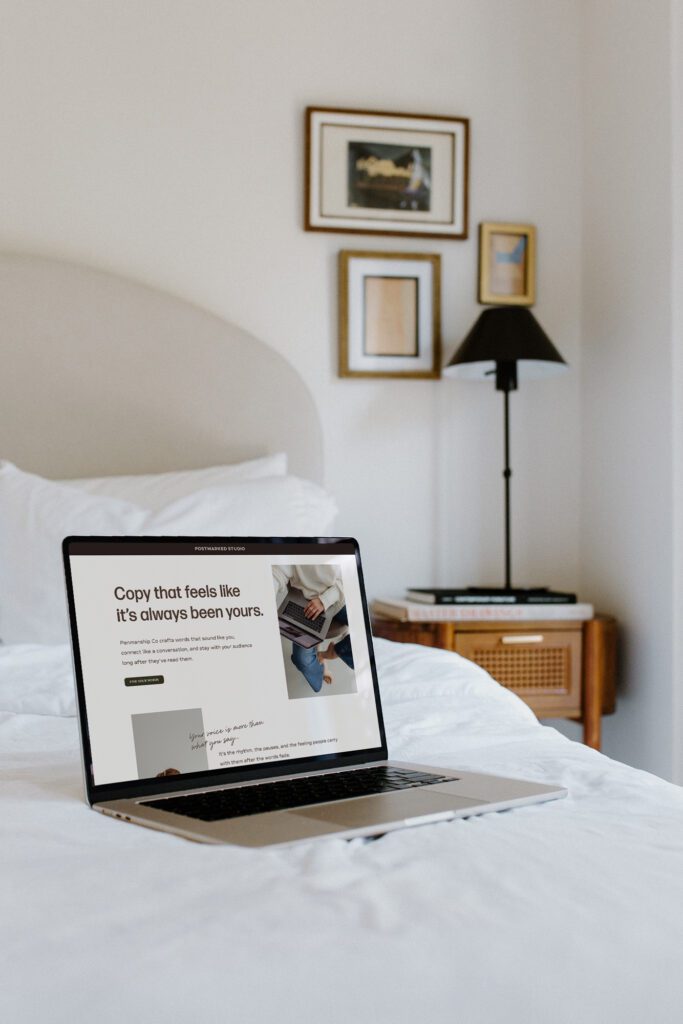 Laptop open to a copywriter's website sitting on a white bed in the corner of the room.